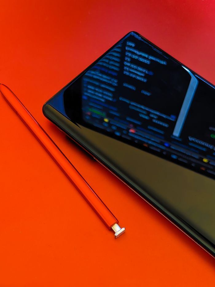 A close view of a smartphone with a stylus resting on a bright red surface, presenting modern technology.